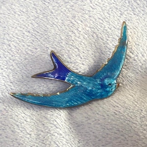 May include: A blue and purple enamel swallow bird brooch. The bird is in flight with its wings spread out. The brooch is made of metal and has a silver finish.