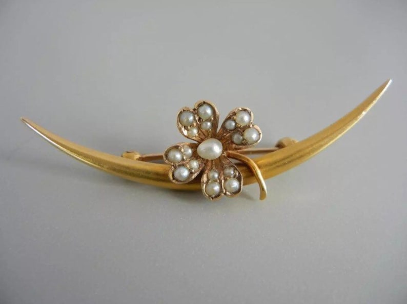 May include: A gold crescent moon brooch with a four-leaf clover design set with pearls.