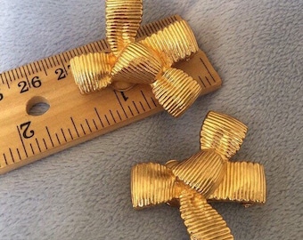 May include: Two gold-toned bow-shaped hair clips. The clips are about 1 inch wide and have a ribbed texture.