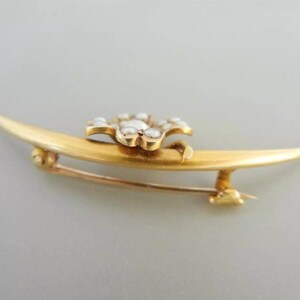 May include: A gold crescent moon brooch with a flower-shaped center set with white pearls.