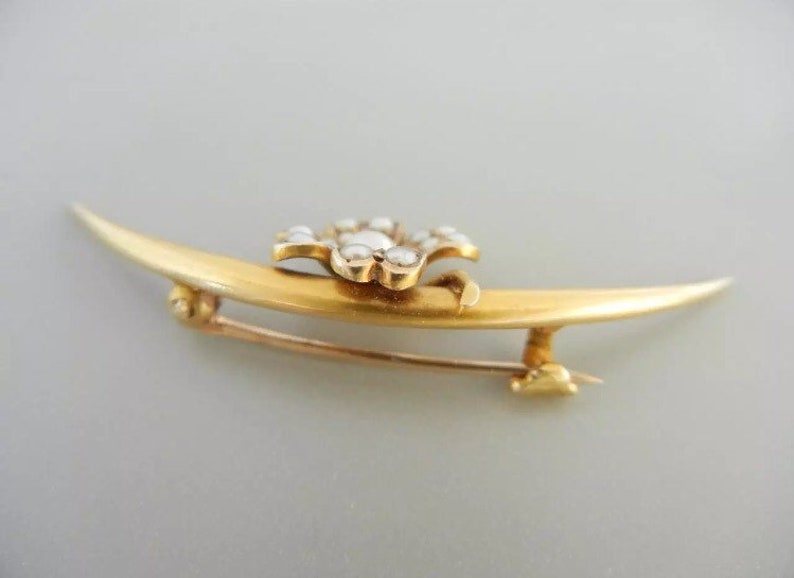 May include: A gold crescent moon brooch with a flower-shaped center set with white pearls.