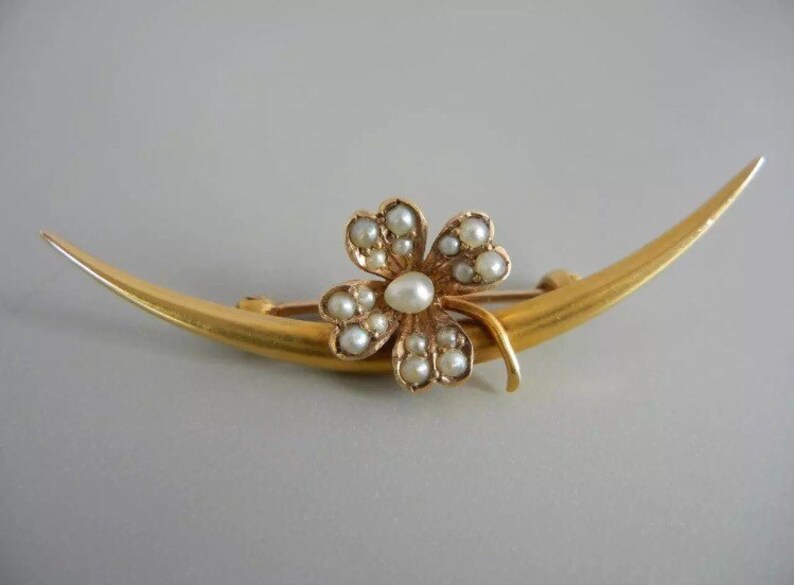 May include: A gold crescent moon brooch with a four-leaf clover design set with pearls.