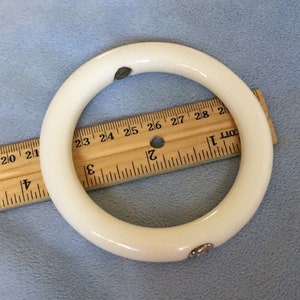 Puede incluir: Pulsera blanca de tipo bangle con detalles plateados. La pulsera mide aproximadamente 6,35 cm de diámetro.