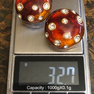 May include: Two amber-colored, round earrings with gold accents and clear rhinestones. The earrings are on a digital scale that reads 3.27 grams. Capacity: 1000gX0.1g