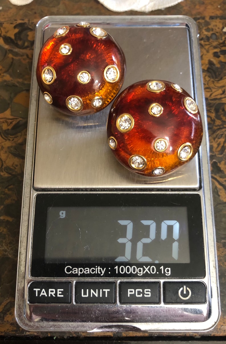 May include: Two amber-colored, round earrings with gold accents and clear rhinestones. The earrings are on a digital scale that reads 3.27 grams. Capacity: 1000gX0.1g