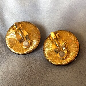 May include: A pair of gold-tone clip-on earrings with a round, textured design. The earrings have a dark, almost black, center.