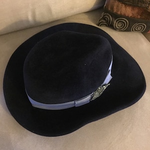 May include: A navy blue felt fedora hat with a light blue ribbon and a silver embellishment.