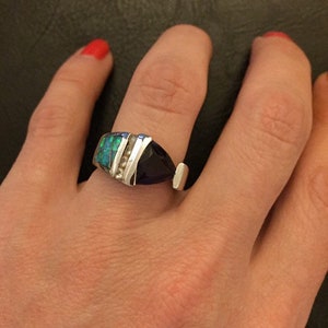 Könnte beinhalten: Ein silberner Ring mit einem großen, tropfenförmigen, dunkelblauen Edelstein. Der Ring hat auch einen rechteckigen Abschnitt mit einem grün-blauen, opalartigen Stein und kleinen, klaren Steinen. Der Ring befindet sich an einem Finger.