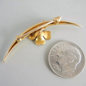 May include: A gold-toned brooch in the shape of a crescent moon with a four-leaf clover design. The brooch is about the size of a dime.
