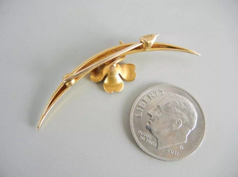 May include: A gold-toned brooch in the shape of a crescent moon with a four-leaf clover design. The brooch is about the size of a dime.