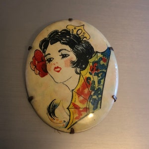 Pu&ograve; includere: Specchio compatto vintage di forma ovale con un'immagine colorata di una donna con un fiore nei capelli e un ventaglio. La donna indossa un vestito a motivi gialli e rossi. Lo specchio ha uno sfondo bianco ed &egrave; decorato con accenti metallici.