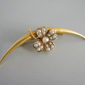 May include: A gold brooch with a crescent-shaped bar and a four-leaf clover design set with pearls.