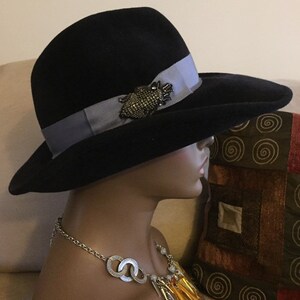 May include: A black felt fedora hat with a wide brim and a light blue ribbon. The hat has a decorative pin with a beaded design.