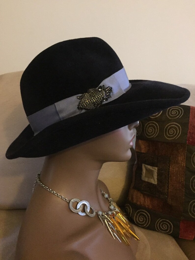 May include: A black felt fedora hat with a wide brim and a light blue ribbon. The hat has a decorative pin with a beaded design.