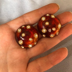May include: A pair of round, brown, resin earrings with gold accents and clear rhinestones.