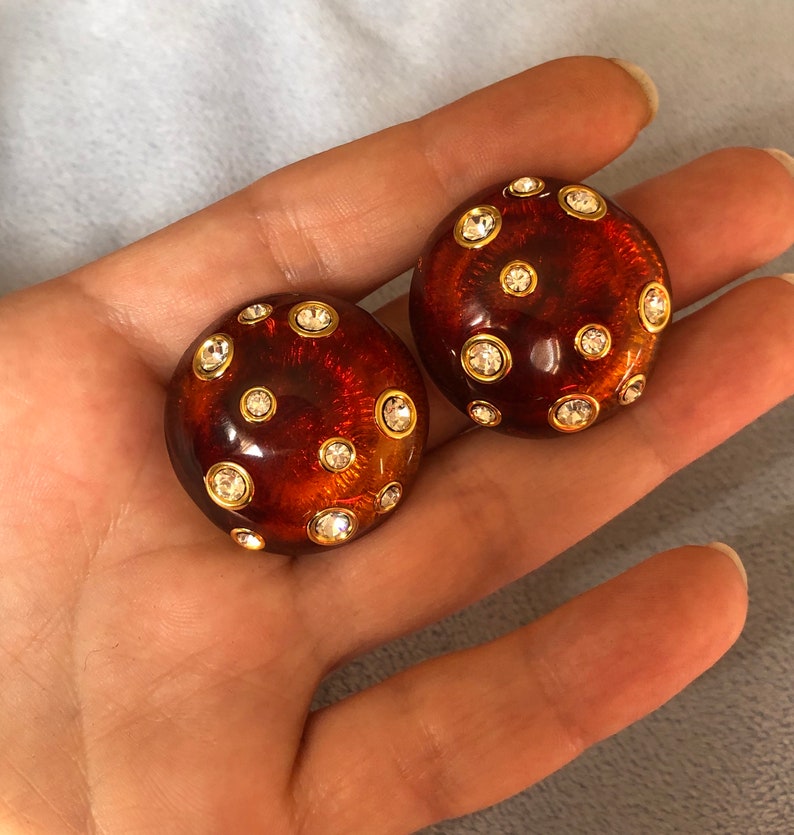 May include: A pair of round, brown, resin earrings with gold accents and clear rhinestones.
