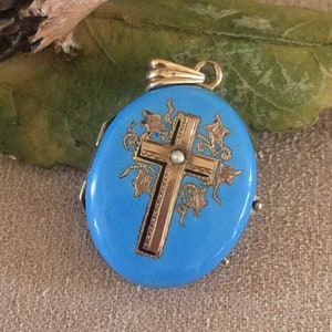 May include: A blue enamel locket with a gold cross and a pearl accent. The locket is decorated with gold ivy vines.