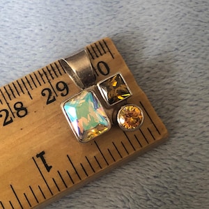 Puede incluir: Un colgante de plata con tres piedras preciosas iridiscentes y ámbar. El colgante mide aproximadamente 2,5 cm de largo.