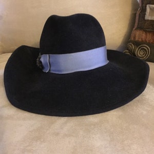 May include: A wide-brimmed navy blue felt hat with a light blue ribbon and a decorative embellishment.