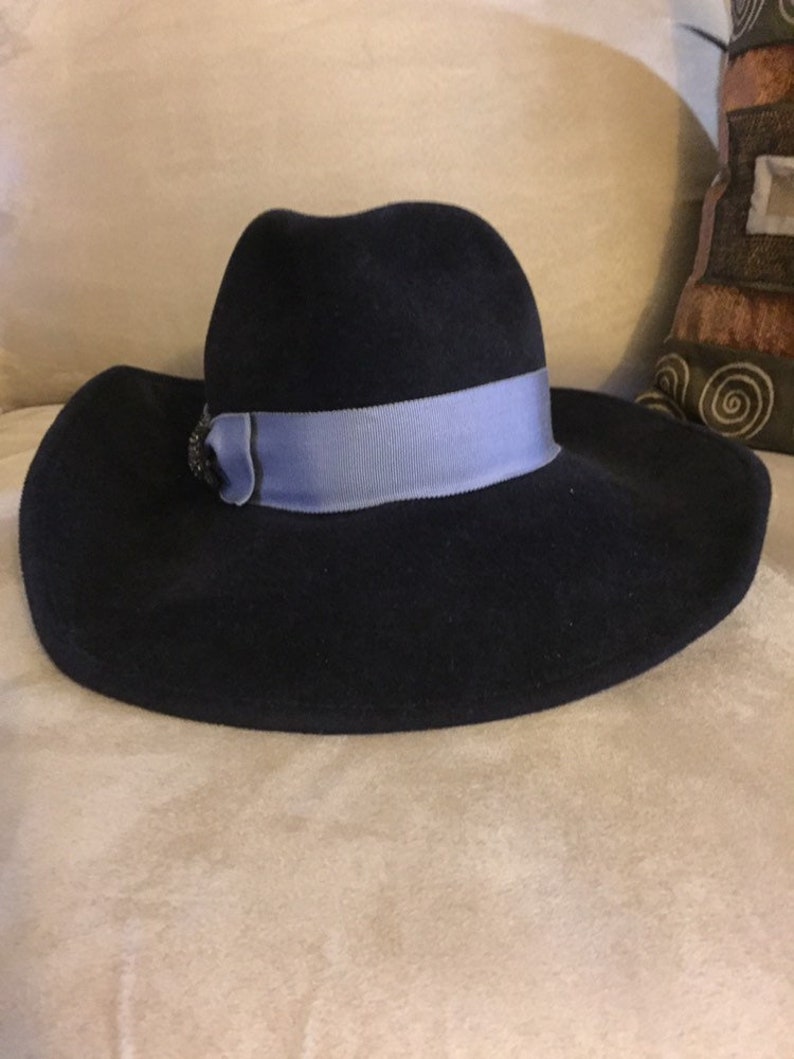 May include: A wide-brimmed navy blue felt hat with a light blue ribbon and a decorative embellishment.