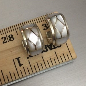 May include: A pair of silver hoop earrings with a white mother-of-pearl inlay. The earrings are approximately 2.5 cm in diameter.