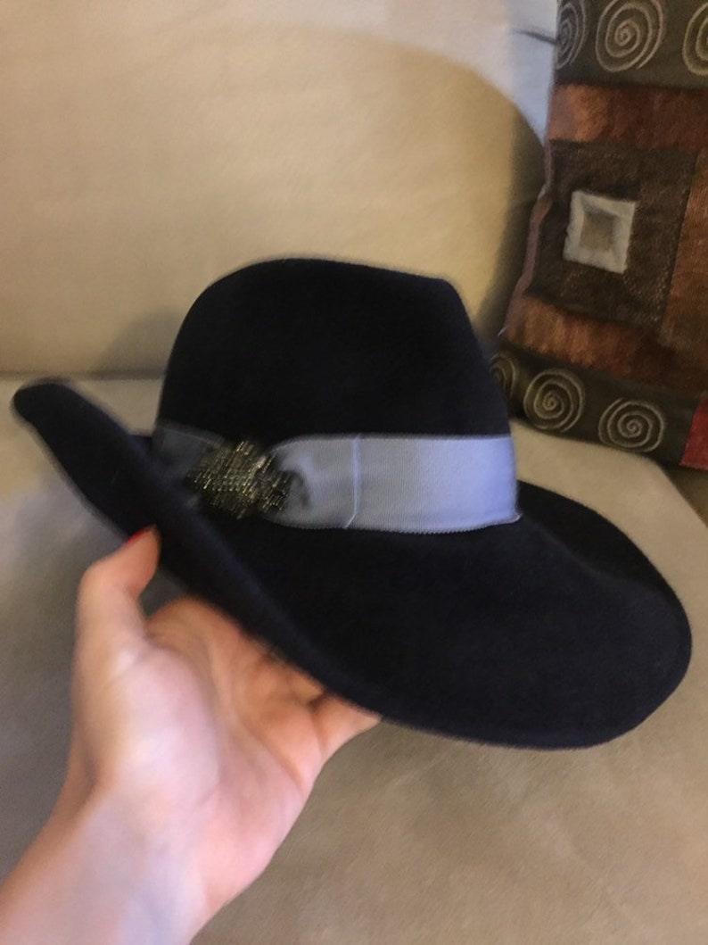 May include: A black felt fedora hat with a wide brim and a light blue ribbon. The hat has a decorative embellishment on the front.