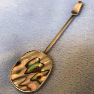 May include: A silver pendant with a long, thin chain. The pendant is oval-shaped and features a mother-of-pearl inlay with iridescent colours.