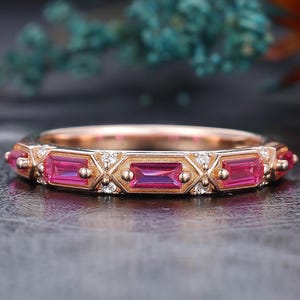 May include: A rose gold ring with a repeating pattern of rectangular pink gemstones and small white accent stones. The ring's design features geometric shapes and a delicate, detailed setting, showcasing a blend of modern and classic styles.