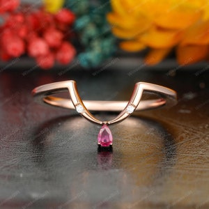 May include: A rose gold ring with a teardrop shaped ruby gemstone and two small diamonds on the band.