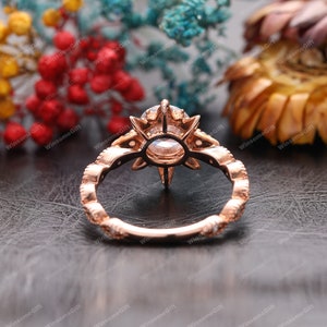 Puede incluir: Un anillo de compromiso de oro rosa con una piedra central grande, redonda y transparente rodeada de piedras m&aacute;s peque&ntilde;as. El anillo tiene un dise&ntilde;o floral delicado con un patr&oacute;n de estrella.