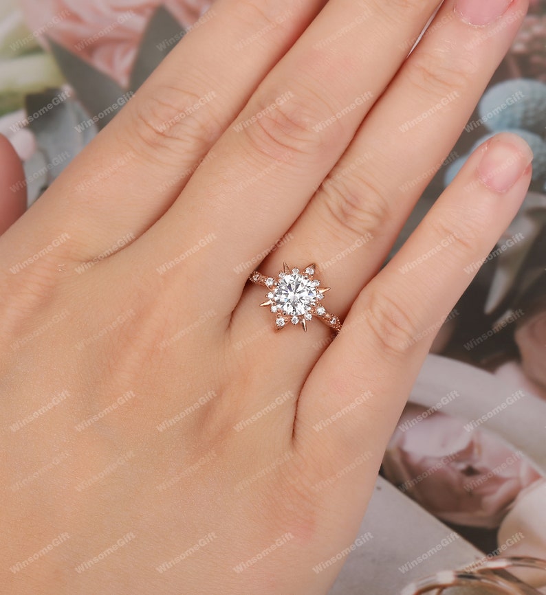 Puede incluir: Un anillo de compromiso de oro rosa con una gran piedra central redonda rodeada de piedras m&aacute;s peque&ntilde;as en un dise&ntilde;o de copo de nieve.