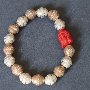 May include: A brown and white beaded bracelet with a red Buddha head charm.