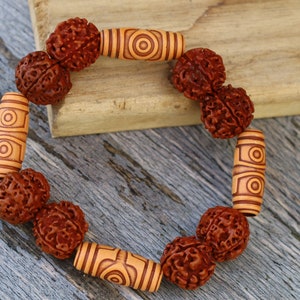 Op de afbeelding: Een bruine houten armband met ronde kralen en cilindrische kralen met ingewikkelde patronen. De armband is gemaakt van natuurlijke materialen en heeft een rustieke uitstraling.