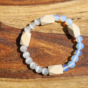 Könnte beinhalten: Ein weißes und blaues Perlenarmband mit Holzperlen. Das Armband besteht aus runden und quadratischen Perlen.