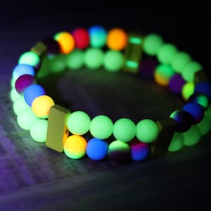 Op de afbeelding: Een glow-in-the-dark armband met groene, gele, blauwe, oranje, rode en paarse kralen. De armband bestaat uit twee rijen kralen, waarbij de buitenste rij groen is en de binnenste rij een mix van kleuren.
