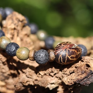 Op de afbeelding: Een armband gemaakt met zwarte lavastenen kralen, bruine houten kralen en een enkele bruine zaadkraal met een patroon.
