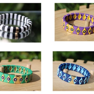 Op de afbeelding: Vier kleurrijke armbanden met een gouden sluiting en een blauw boze oog ontwerp. De armbanden zijn gemaakt van siliconen en hebben een ruitpatroon. De armbanden liggen op een houten oppervlak.