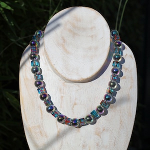 Pode incluir: Um colar de contas de vidro azul e verde iridiscente com contas quadradas intercaladas.