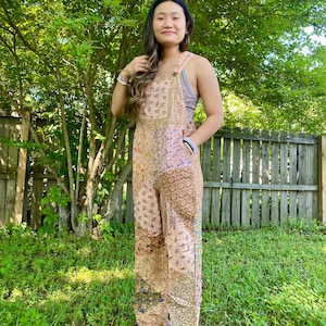 May include: A patchwork jumpsuit in beige, pink, and brown tones. The jumpsuit has floral and geometric patterns. It has adjustable straps and wide legs. The style is bohemian and relaxed, suitable for casual wear.