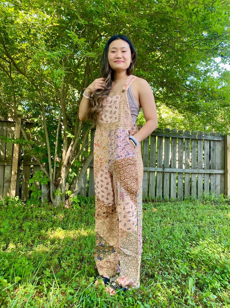 May include: A patchwork jumpsuit in beige, pink, and brown tones. The jumpsuit has floral and geometric patterns. It has adjustable straps and wide legs. The style is bohemian and relaxed, suitable for casual wear.