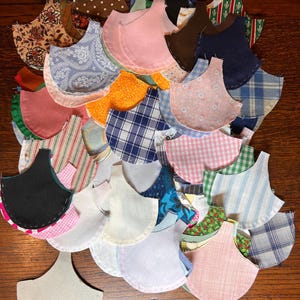 Puede incluir: Una colección de recortes de tela en varios colores y patrones, incluyendo diseños de cuadros, florales y rayas. Los recortes están cortados en forma de media luna y están dispuestos en una pila sobre una superficie de madera.
