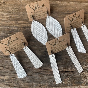 May include: Three pairs of white leather earrings with a chevron pattern. The earrings are on cards with the text "Be Kind" and a heart.