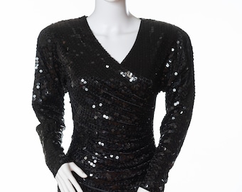 Può includere: Un abito nero di paillettes con scollo a V e maniche lunghe. L'abito ha un corpetto aderente e una gonna fluida.