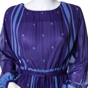 Puede incluir: Vestido largo plisado morado de manga larga, con cuello redondo y cinturón a juego. El vestido presenta rayas verticales azul claro y lunares en el corpiño y las mangas. Los puños son de color azul claro.