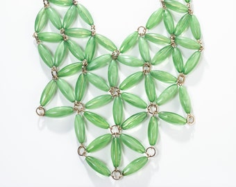 Può includere: Una collana di perline di vetro verde con una catena dorata. Le perline sono disposte in un motivo geometrico, creando un design delicato e intricato.