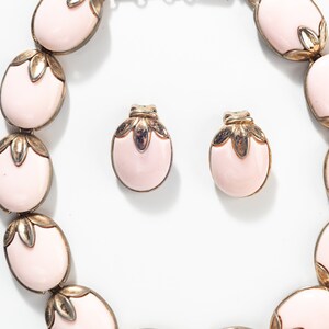 Puede incluir: Un conjunto de collar y pendientes de color rosa y dorado. El collar est&aacute; hecho de piedras rosas ovaladas con detalles dorados. Los pendientes tambi&eacute;n son ovalados y tienen un dise&ntilde;o similar.