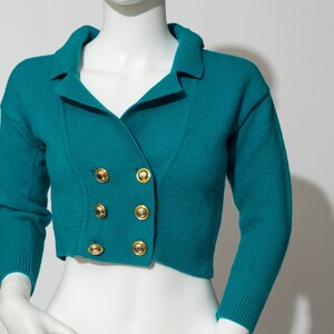 May include: Teal blue cropped cardigan with a double breasted closure and gold buttons.