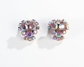 Può includere: Un paio di orecchini di strass iridescenti viola e blu. Gli orecchini sono in metallo dorato e hanno un gruppo di strass al centro.