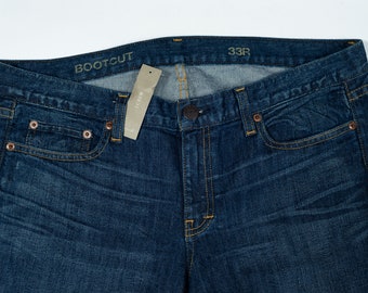 Può includere: Un paio di jeans in denim blu scuro con apertura gamba a zampa d'elefante. I jeans hanno un'etichetta in pelle marrone con il testo "BOOTCUT" e un'etichetta bianca con il testo "J.CREW" sulla cintura. L'etichetta di taglia sulla cintura indica "33R".