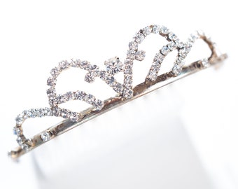 Può includere: Una tiara d'argento con strass trasparenti, progettata in una forma delicata e curva.
